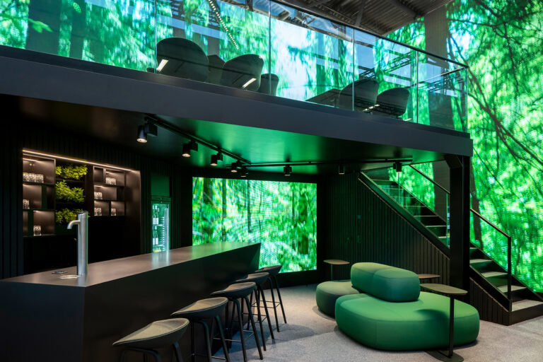 Der Messestand „Servus Future“ für Becken auf der Expo Real präsentiert ein visionäres Raumkonzept von BRÜCKNERINNEN. Ein zweigeschossiger Pavillon aus dunklen Strukturen und transluzenten Flächen verbindet Architektur, Marke und Nachhaltigkeit zu einem immersiven Erlebnis. Großflächige LED-Wände mit dynamischen Naturmotiven schaffen eine Atmosphäre zwischen Digitalität und Natürlichkeit. Der offene Bar- und Loungebereich mit satten Grüntönen, warmem Licht und klarer Formensprache symbolisiert die Zukunft des urbanen Bauens – nachhaltig, kommunikativ, zukunftsorientiert.